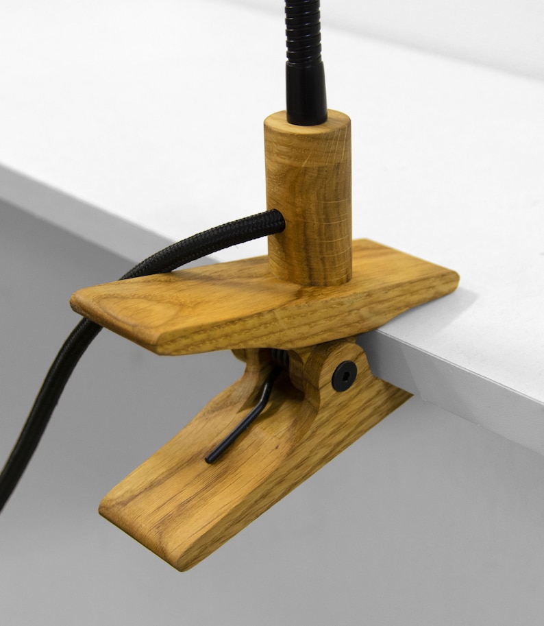 May include: A wooden desk lamp with a black cord and a clamp to attach to a desk or table. The lamp has a flexible arm and a black metal shade.