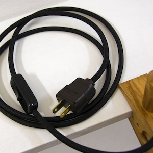 May include: Black electrical cord with a black inline switch and a black plug. The cord is coiled and the plug is visible.