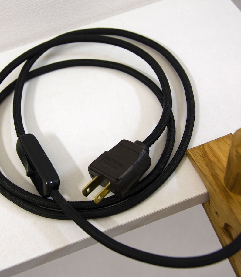 May include: Black electrical cord with a black inline switch and a black plug. The cord is coiled and the plug is visible.