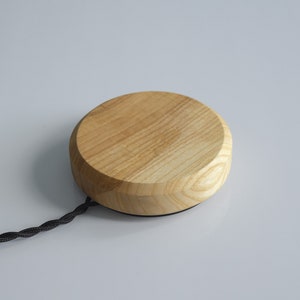 May include: A round wooden base with a black cord attached. The base is made of light wood with a natural grain pattern.