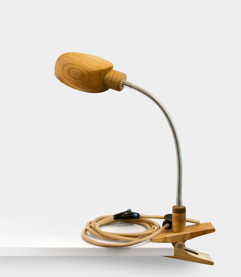 May include: A wooden desk lamp with a flexible gooseneck arm and a clamp base. The lamp has a natural wood finish and a beige cord.