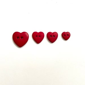 May include: Four red heart-shaped buttons of different sizes. The buttons have two holes each.