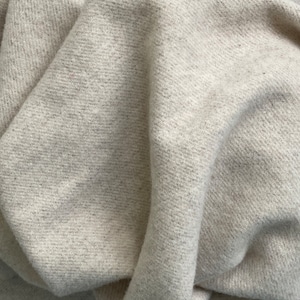 May include: Close-up of a cream-colored woven fabric with a textured surface. The fabric is folded and draped, showing the soft, natural texture.