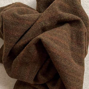 May include: A brown wool fabric with a subtle plaid pattern. The fabric is soft and has a slightly fuzzy texture.