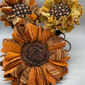 May include: Three felt sunflowers with brown centers and brown button accents. The sunflowers are arranged on a metal wire stand.