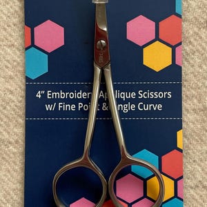 May include: Silver 4-inch embroidery and applique scissors with a fine point and angled curve. The scissors are on a blue background with colorful hexagonal shapes. The packaging says "FAMORÉ" and "Quality Tools for Creative Minds".