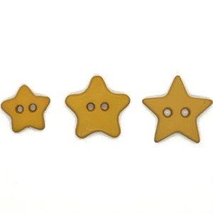 May include: Three gold star-shaped buttons with two holes each. The buttons are different sizes.