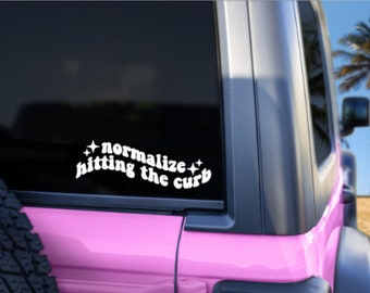 May include: A pink car with a white vinyl sticker on the back window that says "normalize hitting the curb" with stars on either side of the text.