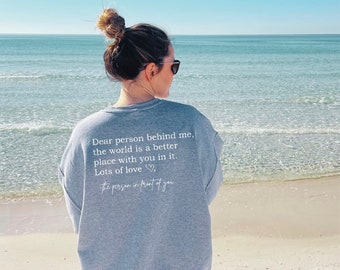 Puede incluir: Una sudadera gris con un mensaje blanco en la espalda que dice "Querida persona detrás de mí, el mundo es un lugar mejor contigo en él. Mucho amor, la persona delante de ti".