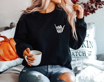 Könnte beinhalten: Schwarzes Sweatshirt mit Rundhalsausschnitt und einem weißen Skelett-Hand-Motiv auf der Brust. Das Sweatshirt ist einfarbig schwarz und hat lange Ärmel. Die Grafik ist eine stilisierte Darstellung einer Hand, die das "Hang Loose"-Zeichen macht.