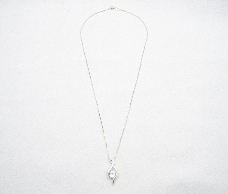 May include: A silver chain necklace with a clear crystal pendant. The pendant is a simple, elegant design with a single crystal set in a silver setting.