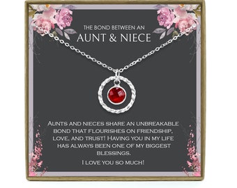 May include: A silver necklace with a red gemstone pendant in a gift box. The box has a floral design and the text "The bond between an aunt & niece" and "AUNTS AND NIECES SHARE AN UNBREAKABLE BOND THAT FLOURISHES ON FRIENDSHIP, LOVE, AND TRUST! HAVING YOU IN MY LIFE HAS ALWAYS BEEN ONE OF MY BIGGEST BLESSINGS. I LOVE YOU SO MUCH!"