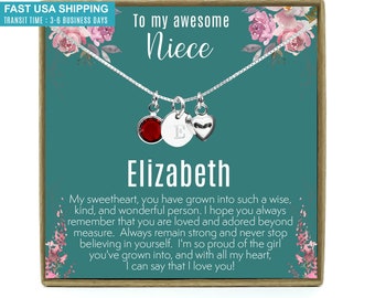May include: A teal blue gift box with a silver necklace inside. The necklace has a red gemstone, a silver heart charm, and a silver charm with the letter "E". The box has a floral design and the text "To my awesome Niece Elizabeth" on the front.