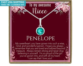 May include: A gift box with a silver necklace and a teal gemstone pendant. The box has a burgundy background with pink floral accents and the text "To my awesome Niece Penelope".