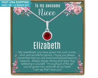 May include: A silver necklace with a round, red gemstone pendant, presented on a teal card with floral accents. The card reads "To my awesome Niece" and includes the name "Elizabeth" and a heartfelt message.