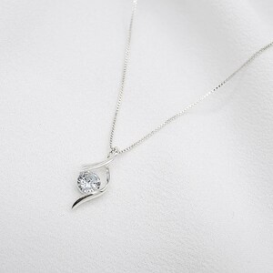 May include: A silver necklace with a delicate chain and a single, clear, round gemstone pendant. The pendant is set in a simple, elegant design.