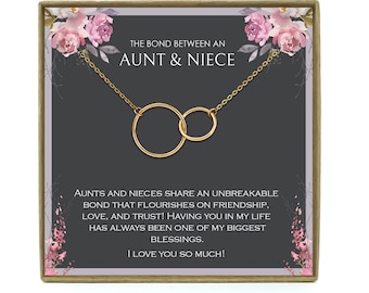 May include: A gold necklace with two interlocking circles in a gift box. The box has a gray background with pink floral accents and the text "The bond between an aunt & niece."  The text below the necklace reads "AUNTS AND NIECES SHARE AN UNBREAKABLE BOND THAT FLOURISHES ON FRIENDSHIP, LOVE, AND TRUST! HAVING YOU IN MY LIFE HAS ALWAYS BEEN ONE OF MY BIGGEST BLESSINGS. I LOVE YOU SO MUCH!"