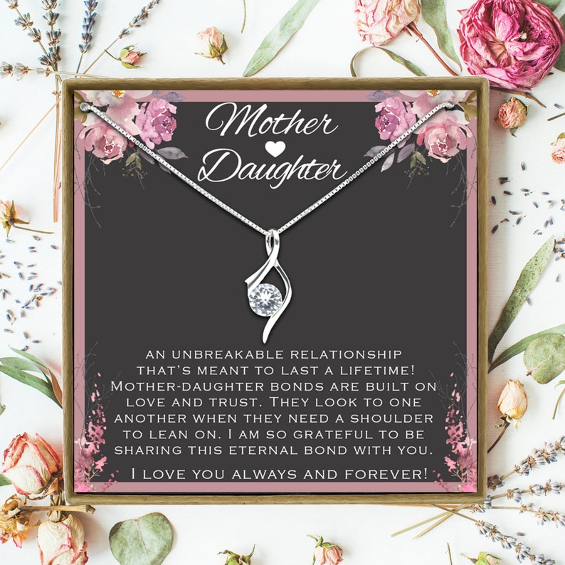 May include: A silver necklace with a clear crystal pendant and a card that reads "Mother Daughter" with a pink heart. The card has a floral design and the text "An unbreakable relationship that's meant to last a lifetime! Mother-daughter bonds are built on love and trust. They look to one another when they need a shoulder to lean on. I am so grateful to be sharing this eternal bond with you. I love you always and forever!"