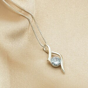 May include: A silver necklace with a delicate, twisted design and a clear, round gemstone pendant.