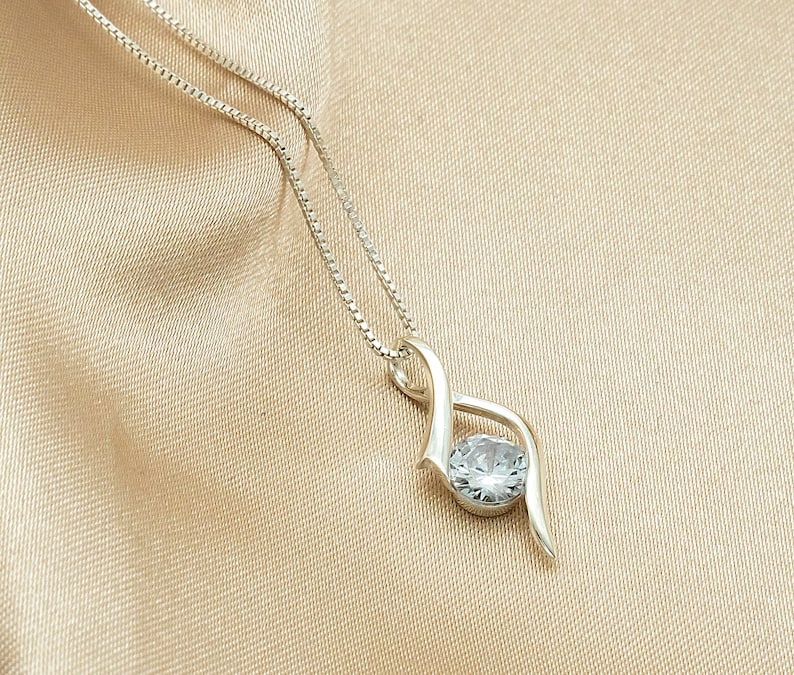May include: A silver necklace with a delicate, twisted design and a clear, round gemstone pendant.