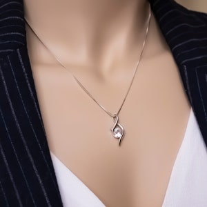 May include: A silver necklace with a delicate pendant featuring a clear gemstone. The pendant is shaped like a stylized infinity symbol.