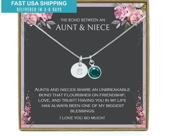May include: A silver necklace with a small round charm engraved with the letter "S" and a green crystal charm. The necklace is in a gift box with a floral design and the text "The bond between an aunt & niece" and "AUNTS AND NIECES SHARE AN UNBREAKABLE BOND THAT FLOURISHES ON FRIENDSHIP, LOVE, AND TRUST! HAVING YOU IN MY LIFE HAS ALWAYS BEEN ONE OF MY BIGGEST BLESSINGS. I LOVE YOU SO MUCH!"