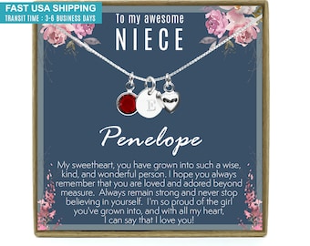 May include: A silver necklace with a red crystal charm, a heart charm, and a charm with the letter "E". The necklace is in a blue box with a floral design and the text "To my awesome NIECE Penelope". The box also includes the text "My sweetheart, you have grown into such a wise, kind, and wonderful person. I hope you always remember that you are loved and adored beyond measure. Always remain strong and never stop believing in yourself. I'm so proud of the girl you've grown into, and with all my heart, I can say that I love you!"