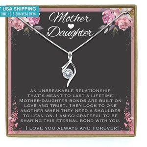 May include: A silver necklace with a clear crystal pendant in a gift box. The box has a floral design and the text "Mother Daughter" with a heart symbol. The text inside the box reads "An unbreakable relationship that's meant to last a lifetime! Mother-daughter bonds are built on love and trust. They look to one another when they need a shoulder to lean on. I am so grateful to be sharing this eternal bond with you. I love you always and forever!"
