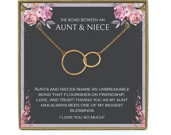 May include: A gold necklace with two interlocking circles, presented in a gift box with a floral design. The box features the text "The bond between an aunt & niece" and a message about the unbreakable bond between aunts and nieces.