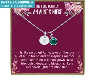 May include: A silver necklace with a small silver disc charm with the letter "S" and a green gemstone charm. The necklace is in a burgundy box with a floral design and the text "The bond between an aunt & niece".