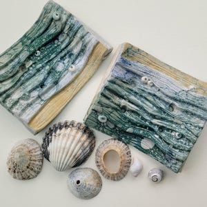 May include: Two ceramic soap dishes with a green and white wave pattern. The dishes are decorated with small white dots. There are six seashells of various sizes and colours next to the dishes.