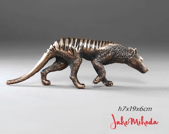 May include: Bronze sculpture of a Tasmanian tiger, a now extinct marsupial, walking with its head turned to the side. The sculpture is 7 inches tall, 19 inches long, and 6 inches wide.  h7x19x6cm Jake Mikoda