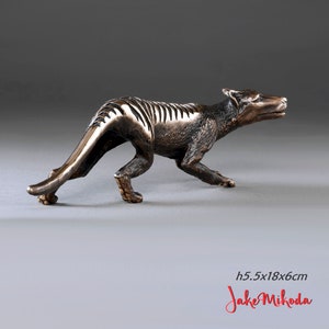 May include: Bronze sculpture of a Tasmanian tiger, a carnivorous marsupial that is now extinct. The sculpture is 5.5 inches tall, 18 inches long, and 6 inches wide. The sculpture is in a walking pose, with its head turned to the right. The sculpture is made of bronze and has a dark brown patina.