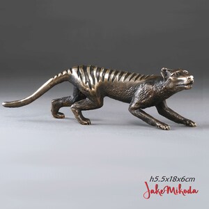 May include: Bronze sculpture of a Tasmanian tiger, also known as a thylacine, in a crouching position. The sculpture is 5.5 inches tall, 18 inches long, and 6 inches wide. The sculpture is signed "Jake Mikoda".