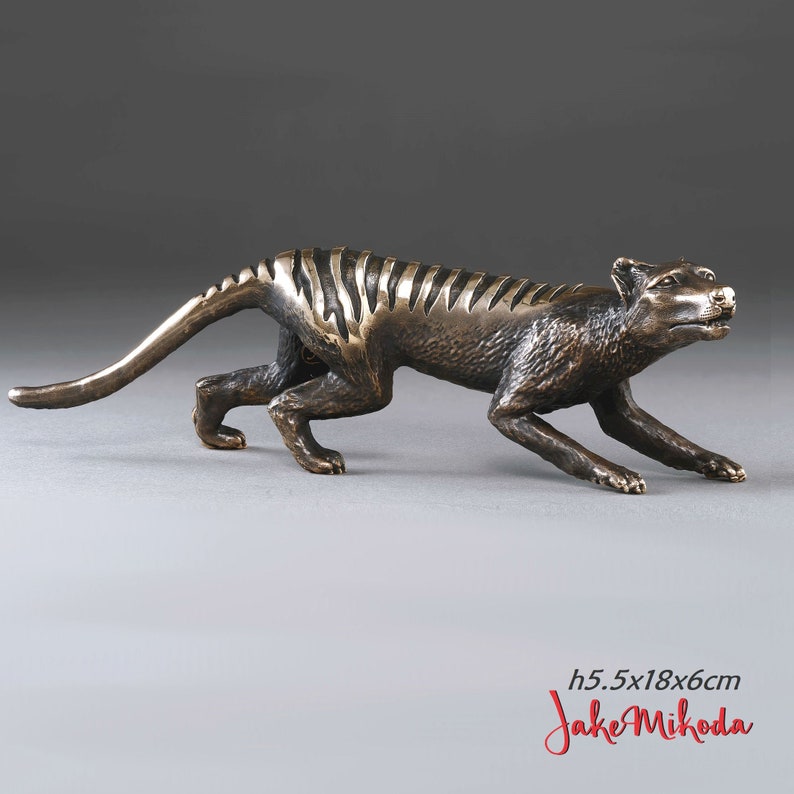 May include: Bronze sculpture of a Tasmanian tiger, also known as a thylacine, in a crouching position. The sculpture is 5.5 inches tall, 18 inches long, and 6 inches wide. The sculpture is signed "Jake Mikoda".