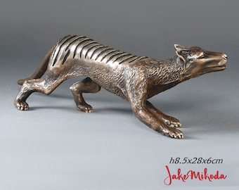 May include: A bronze sculpture of a thylacine, also known as a Tasmanian tiger, in a stalking pose. The sculpture is 8.5cm high and 28cm long. The thylacine has a striped back and a long tail. The artist's name, Jake Mihoda, is in red script.