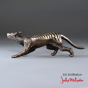 May include: Bronze sculpture of a Tasmanian tiger, also known as a thylacine, in a running pose. The sculpture is 5.5 inches tall, 18 inches long, and 6 inches wide. The sculpture is signed "Jake Mikoda".