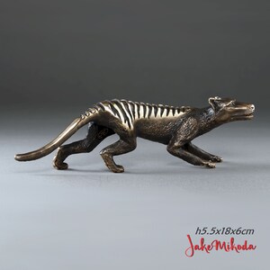 May include: Bronze sculpture of a Tasmanian tiger, also known as a thylacine, in a running pose. The sculpture is 5.5 inches tall, 18 inches long, and 6 inches wide. The sculpture is signed "Jake Mikoda".