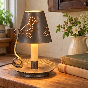 May include: A metal table lamp with a weathered gray finish, featuring a conical shade with punched-out bird designs. The lamp has a circular base with a fluted edge, a central pillar, and a decorative curved handle on the side.