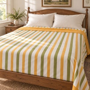 May include: A bed featuring a wooden headboard and frame, dressed in a white, olive green, and mustard yellow vertical striped bedspread. Two plain white pillows are positioned against the headboard, completing the bedding set arrangement.