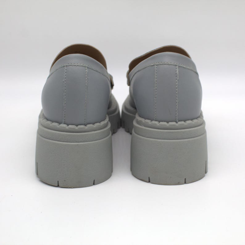Pu&ograve; includere: Un paio di scarpe grigie con plateau e suola spessa. Le scarpe hanno la punta arrotondata e un cinturino sulla parte superiore. La suola platform &egrave; alta circa 7.6 cm. Le scarpe sono realizzate in materiale sintetico liscio.