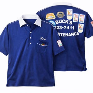 May include: A navy blue polo shirt with a white collar and trim. The shirt has a pocket with a logo and the name "Herb" embroidered above it. The back of the shirt features the text "BUCK'S 123-7411 MAINTENANCE" and several patches.