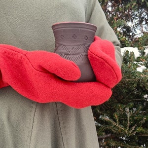 May include: A pair of red fleece mittens holding a brown ceramic mug with a geometric design.