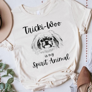 May include: A beige t-shirt with black text that reads "Tricki-Woo is my Spirit Animal" and a black and white illustration of a Pekingese dog.