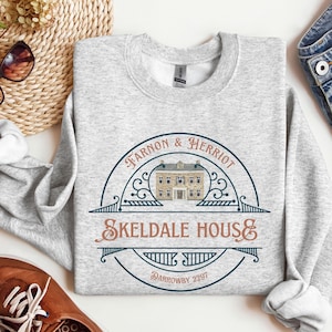 May include: Gray sweatshirt with a navy blue and white graphic of a house with the text "Tarnon & Herriot Skeldale House Darrowby 2297".