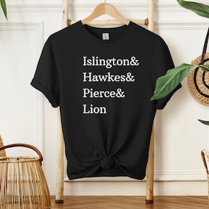 以下が含まれることがあります： 白い文字で「Islington & Hawkes & Pierce & Lion」と書かれた黒いTシャツ