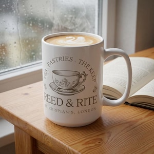 Puede incluir: Una taza de cerámica blanca llena de café con un diseño de arte latte de cisne. La taza muestra un gráfico marrón de una taza de té sobre un platillo con el texto: TEA. PASTRIES. THE KEEP REED & RITE ST. CRISPIAN'S, LONDON en disposición circular.