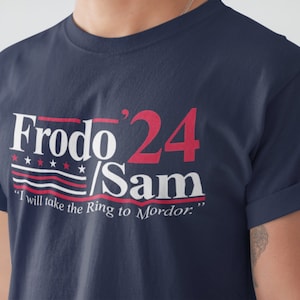 May include: A navy blue t-shirt with a white and red graphic design that says "Frodo 24/Sam" with five stars above the text and a red, white, and blue striped design below the text. The text below the graphic says "I will take the Ring to Mordor."