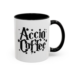 Puede incluir: Taza de cerámica blanca con borde y asa negros. La taza tiene un gráfico negro que dice "Accio Coffee" con estrellas y un rayo.