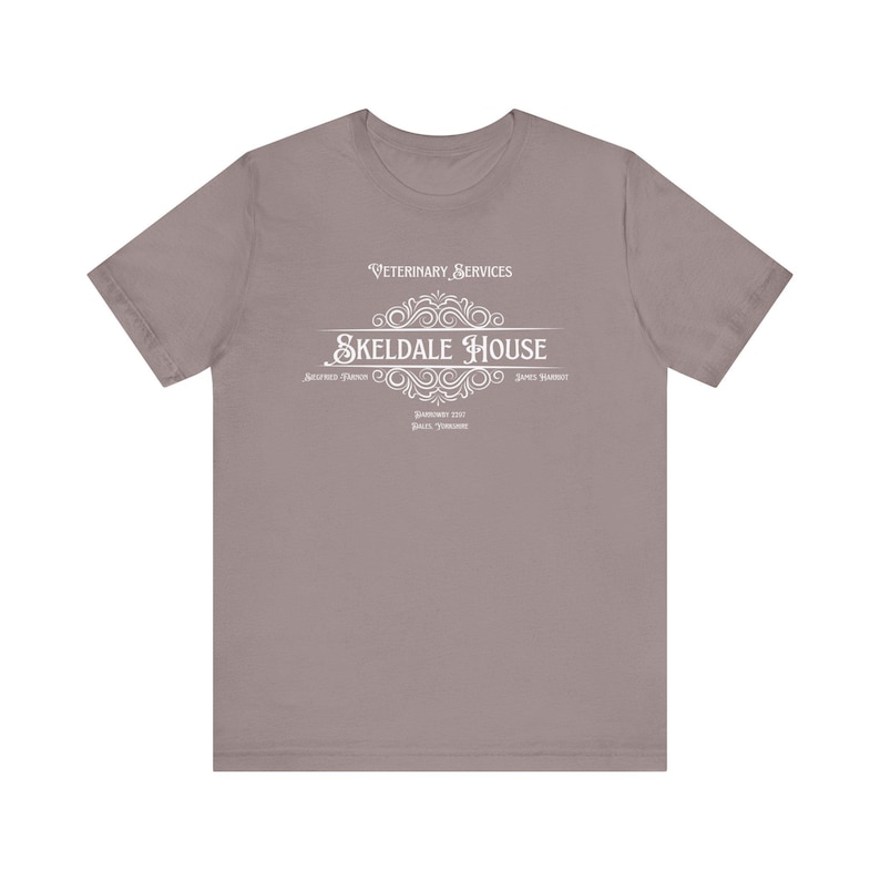 K&ouml;nnte beinhalten: Ein heidefarbenes T-Shirt mit einem wei&szlig;en Grafikdesign, auf dem "Veterinary Services Skeldale House" mit einem dekorativen Schn&ouml;rkel steht. Der Text unter der Grafik lautet "Antiquated Tradition - James Harrison - Downworthy 1921 - Braith, Yorkshire."